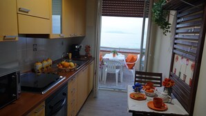 Une cuisine compacte avec vue sur la mer, un coin repas avec une table et des chaises, et un balcon doté d’une balustrade en bois.
