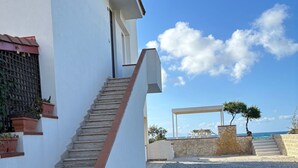 Un bâtiment avec un escalier menant à une porte, un chemin de gravier et une vue sur la mer.