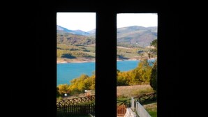 Vista a través de una ventana mostrando un paisaje montañoso con un lago y una cerca de madera al frente.