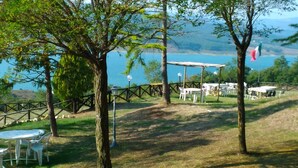 Un espacio al aire libre con mesas y sillas, una pérgola y vistas a un lago y colinas.