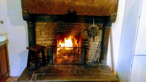 Una chimenea con fuego, un taburete de madera y una reja de metal.