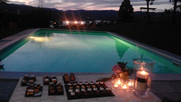 Una piscina con vista al atardecer, velas y pequeños postres en el borde.