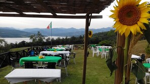 An outdoor dining area with tables and chairs, a sunflower decoration, and a view of a lake and mountains in the background. - Villa park pool exclusively vacation private parties groups up to 35 seats (sansepolcro (arezzo))