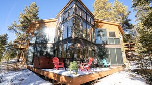 A modern house with a large glass facade, a deck with outdoor seating, and a snowy landscape.