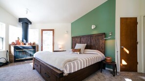A bedroom with a large bed, a fireplace, a green accent wall, and a wooden door.