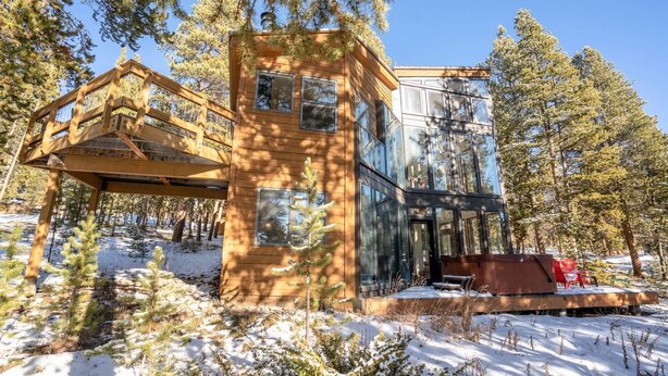 A wooden cabin with a glass extension, surrounded by snow and trees.