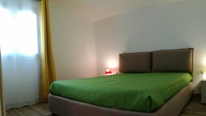 Une chambre à coucher avec un grand lit, une table de chevet, une lampe et une fenêtre avec des rideaux.