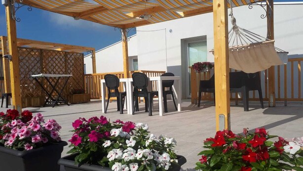 Une terrasse extérieure avec une pergola en bois, des chaises noires, une table et des plantes en pot.