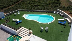 Une piscine entourée d’une pelouse bien entretenue, agrémentée de plusieurs chaises longues et d’un petit escalier menant à une zone aménagée en terrasse.