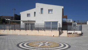 Un bâtiment moderne à la façade blanche, orné d’une mosaïque circulaire au sol et doté d’une balustrade en verre le long du bord.