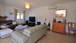 Een woonkamer met een bank, televisie, speakers en een gitaar.