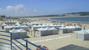 A beach with rows of white tents, a sandy beach, and a clear blue sea.