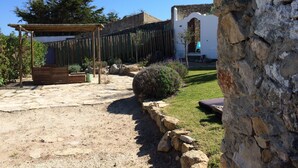 A rustic outdoor area with a wooden pergola, a stone pathway, and a white building with a stone facade.