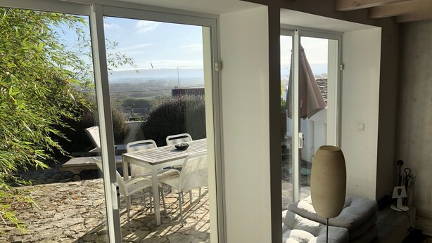 A room with a sliding glass door leading to an outdoor patio with a table and chairs, a sofa, and a lamp.
