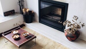 A cozy living room with a fireplace, a wooden table with bowls, a potted plant, and a rug.