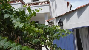 A white building with a red-tiled roof, a stone wall, and a blue door.