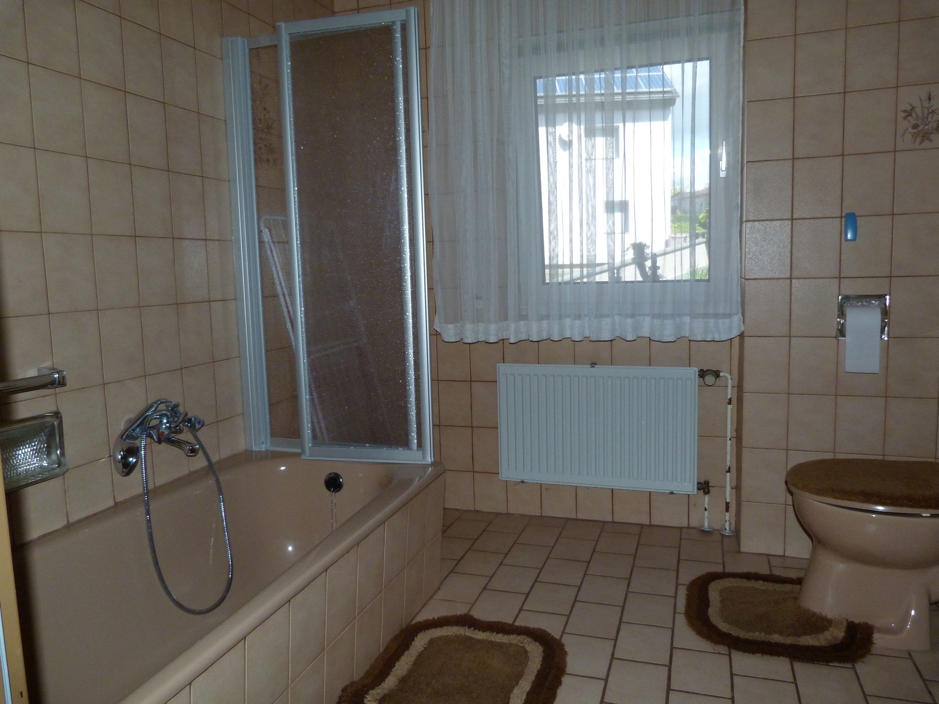 A bathroom with a bathtub, toilet, and a window with a curtain.
