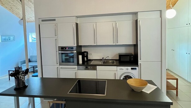 Una cocina moderna con armarios blancos, encimera negra y techo de madera.