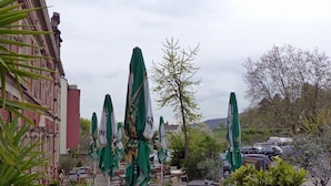 An outdoor seating area with tables and chairs, surrounded by green umbrellas, and a view of parked cars and buildings in the background. - HAARDTER WINZER (Whg. 3) renovated and lovingly decorated "Pfalzcard-Partner" (Neustadt an der Weinstraße)