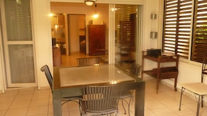 Uma área de refeições com mesa de vidro e cadeiras de metal, um armário de madeira e uma janela com persianas.