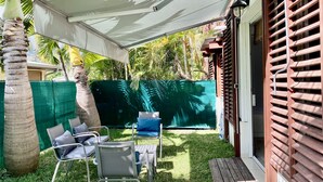 Um espaço de pátio com móveis de exterior, cerca verde e deck de madeira.