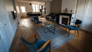 Uma sala de estar ampla, com lareira, área de jantar e cozinha ao fundo.