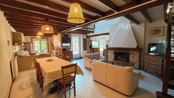 A spacious living area with a fireplace, a dining table, and a kitchen in the background.