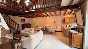 A spacious living area with a staircase, a dining table with chairs, a kitchen area with wooden cabinets, and a white sofa.