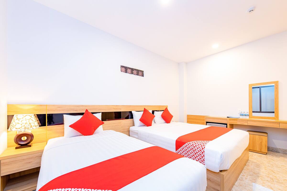 Ein Hotelzimmer mit zwei Betten, einem Nachttisch mit Lampe, einem Spiegel und einem hölzernen Kopfteil.