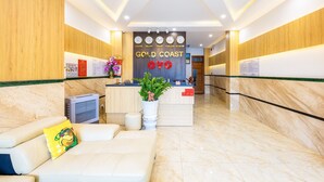 A hotel reception area with a reception desk, a waiting area with a sofa, a potted plant, and a wall displaying the hotel's name and locations.