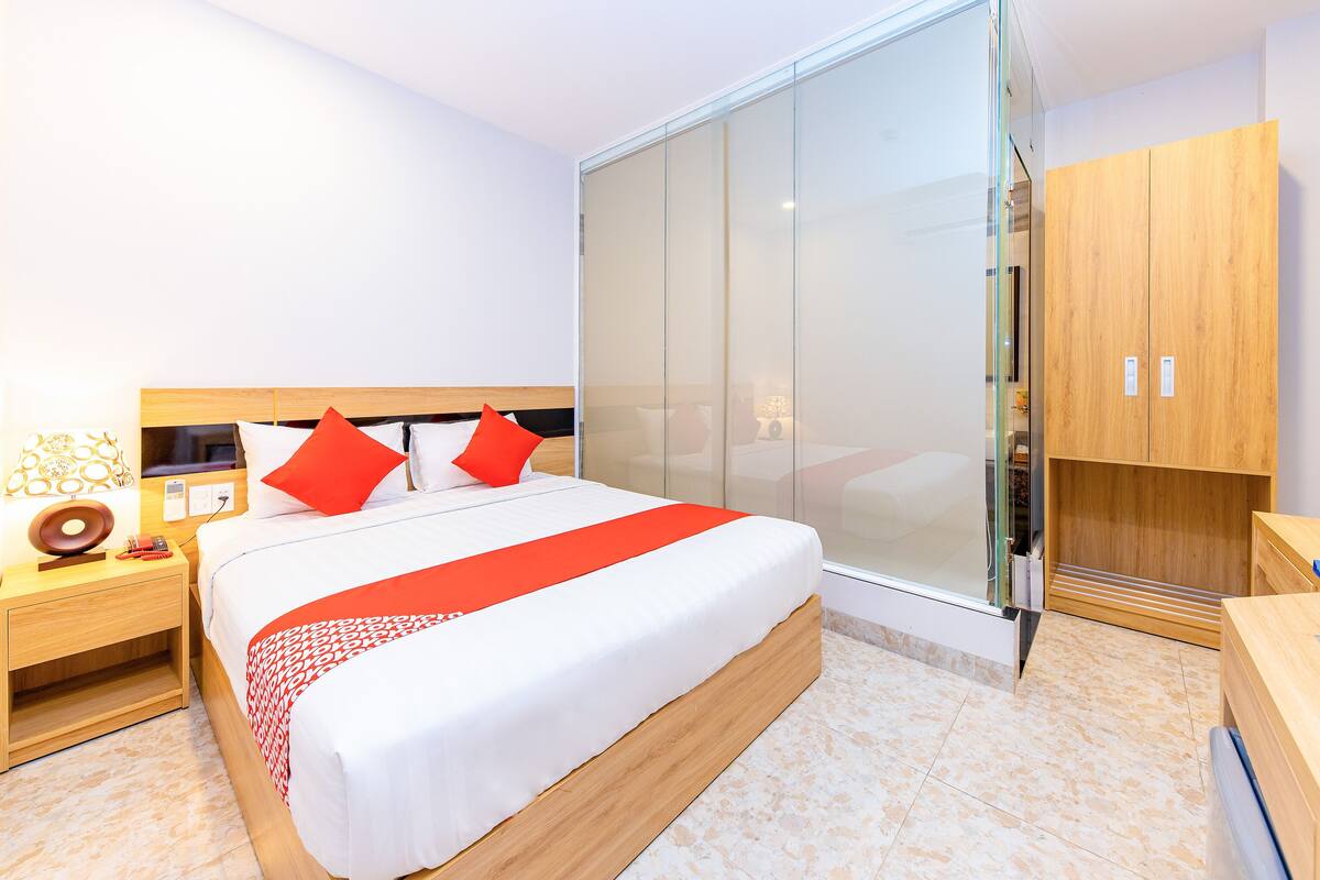 Ein modernes Hotelzimmer mit einem großen Bett, einem Nachttisch aus Holz, einem Glastisch und einem Schrank aus Holz.