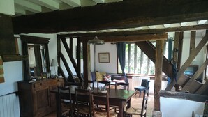 A rustic dining area with a wooden table and chairs, a mirror, and a window with curtains.