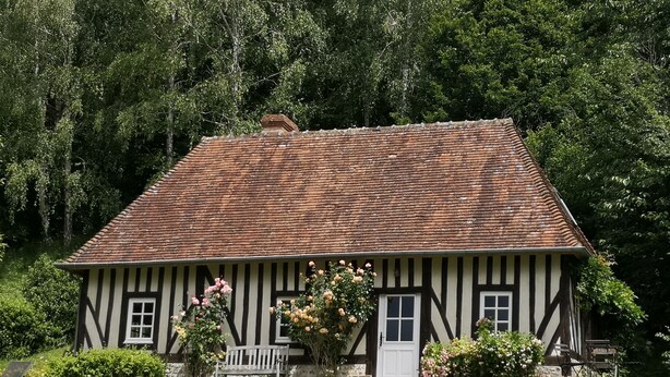 A traditional half-timbered house with a sloped roof, surrounded by lush greenery and a well-maintained lawn.
