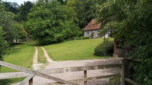 A wooden gate with a sign reading "1601" leading to a house with a red roof, surrounded by lush greenery.