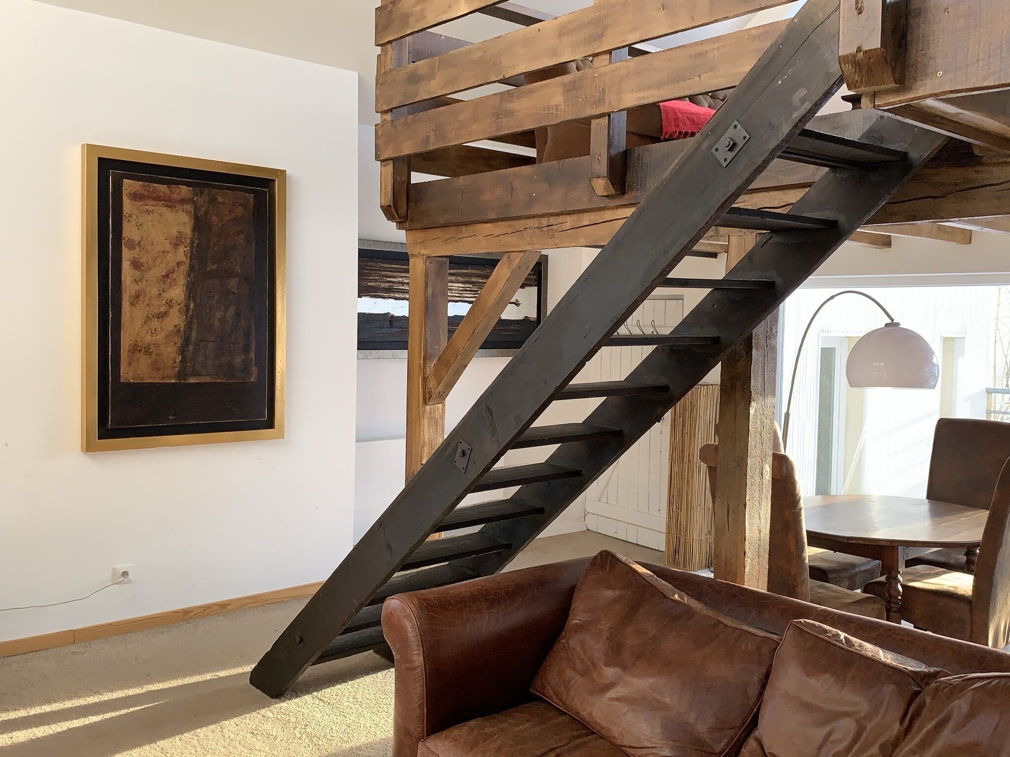 A staircase with a rustic design, a framed artwork on the wall, and a leather sofa in the foreground.