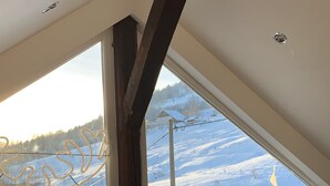 A room with a sloped ceiling, a window with a view of a snowy landscape, and a small table with two candles. - La Traverse, a large family home halfway between Gérardmer and La Bresse. (La Bresse)