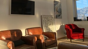 A cozy living room with leather armchairs, a red velvet armchair, a flat-screen TV, and a framed map on the wall. - La Traverse, a large family home halfway between Gérardmer and La Bresse. (La Bresse)