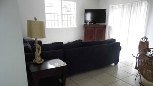 Una sala de estar con un sofá, televisión, lámpara y una silla de mimbre.