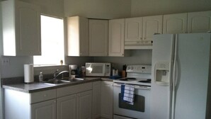 Una cocina con armarios blancos, microondas, estufa, pileta y refrigerador.