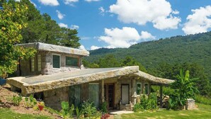 Une maison en pierre dotée d’un grand patio, entourée d’une végétation luxuriante et de collines.