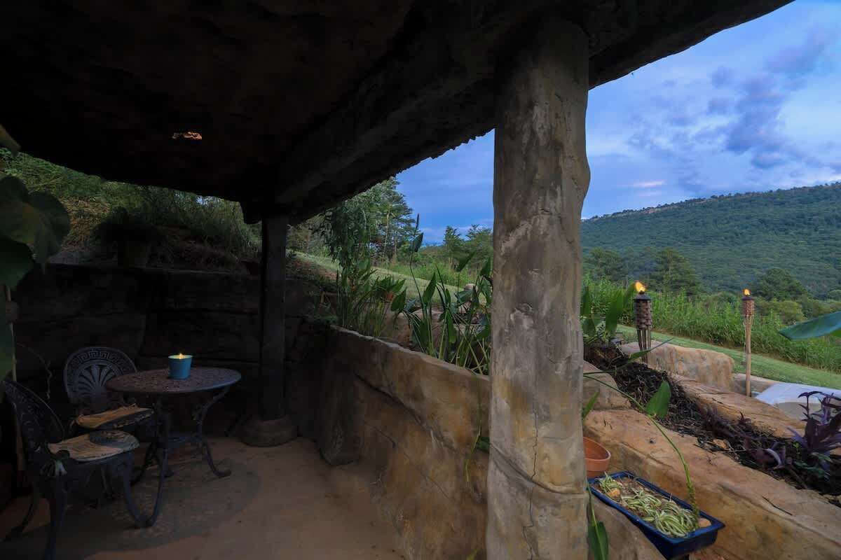 Une terrasse extérieure agrémentée de colonnes en pierre, d’une table ronde et de chaises, offrant une vue sur un paysage verdoyant et luxuriant.