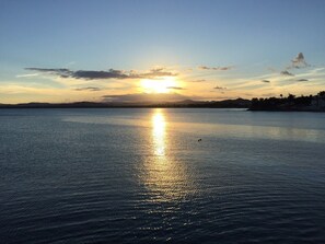 Une étendue d'eau calme où se reflète le soleil, avec une rive lointaine et un ciel dégagé.