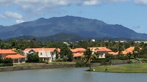A residential area with houses, a body of water, and a mountain in the background. - Ocean Front - 3 Bedroom/3.5 Bath with Terrace Fully Furnished (Humacao)