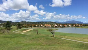 A golf course with a lake, houses in the background, and mountains in the distance. - Ocean Front - 3 Bedroom/3.5 Bath with Terrace Fully Furnished (Humacao)
