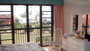 A bedroom with a bed, a chair, a dresser, and a large window with a view of palm trees and a building. - Ocean Front - 3 Bedroom/3.5 Bath with Terrace Fully Furnished (Humacao)