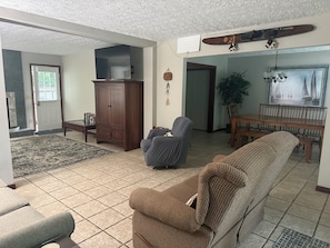 Ein Wohnzimmer mit einer Couch, einem Sessel, einer Holzkommode, einem Esstisch und einer Pendelleuchte.