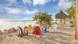 A beach with colorful Adirondack chairs, a thatched-roof structure, and a string of lights.
