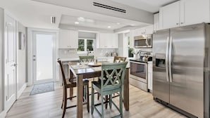 A modern kitchen with white cabinets, stainless steel appliances, and a wooden dining table with chairs.