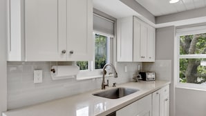 A modern kitchen with white cabinetry, a stainless steel sink, and a window with a view of trees.
