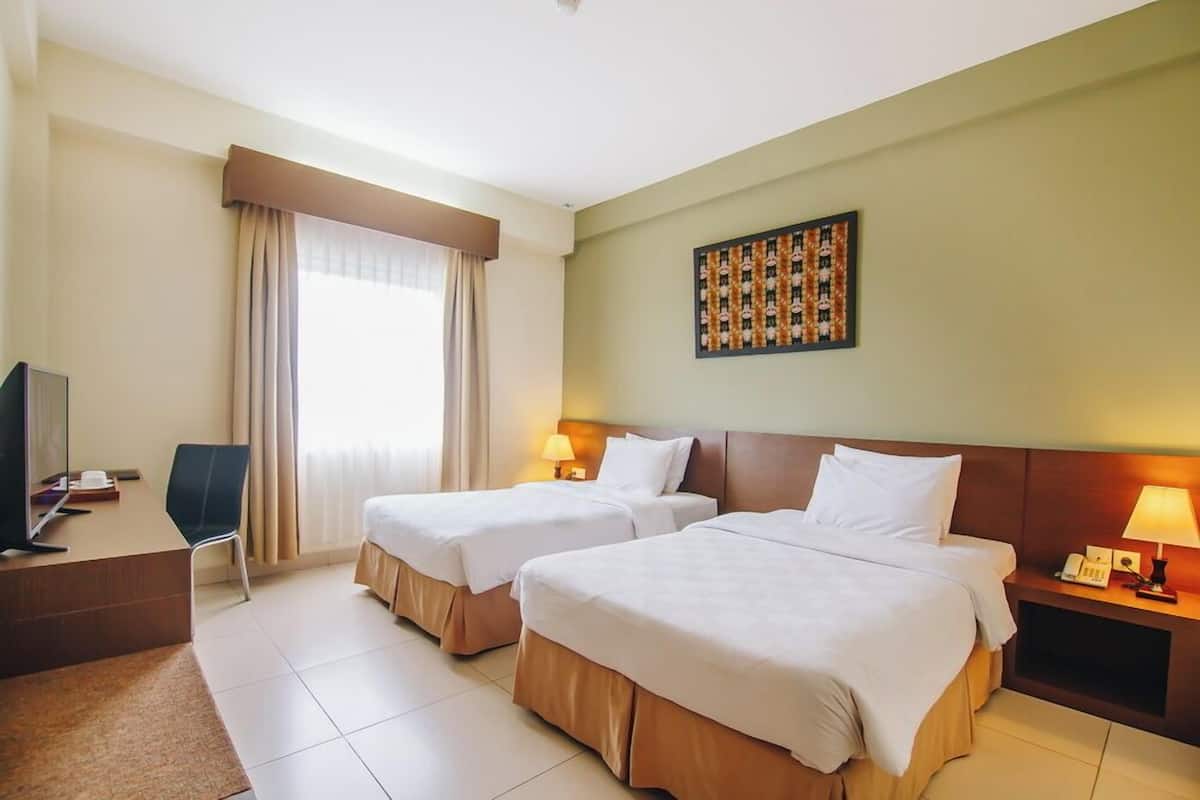A hotel room with two beds, a desk, a chair, a TV, and a painting on the wall.